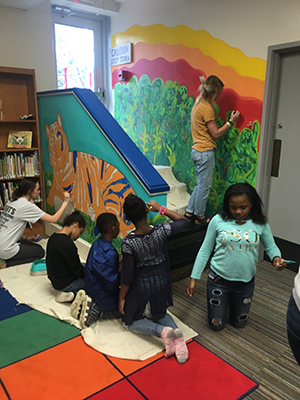 UT students Jacqueline Wright (left) and Kayla Duncan (top) work with students in kindergarten through second grade to complete a mural in the Maynard Elementary School library.